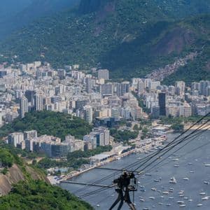 Una funivia viaggia sopra una baia piena di barche, con una città costiera e montagne verdi sullo sfondo.