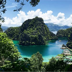 Vue plongeante sur un lagon turquoise entouré d'îles escarpées couvertes de jungle, avec des bateaux amarrés à un ponton en bois.