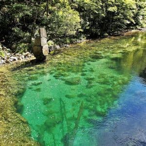 Un fiume limpido e turchese scorre attraverso una foresta lussureggiante e verde, con un pilastro di pietra che si erge sulla riva rocciosa.
