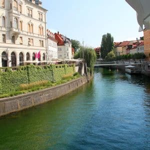 Un canale fluviale serpeggia in città, costeggiato da edifici storici su un lato e da un muro lussureggiante coperto d'edera sull'altro.