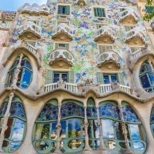Un'inquadratura dal basso della facciata di un edificio, con tessere di mosaico colorate, vetrate istoriate e balconi curvi e ornati.