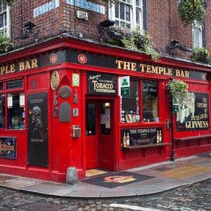 La facciata ad angolo rosso acceso del pub The Temple Bar su una strada di ciottoli bagnata.