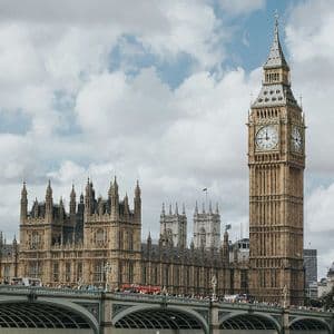 La torre dell'orologio del Big Ben e le Houses of Parliament si ergono dietro un ponte trafficato sotto un cielo nuvoloso.