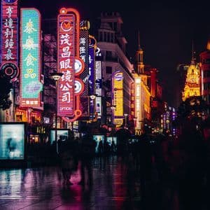 Insegne al neon colorate con caratteri asiatici illuminano una strada cittadina bagnata di notte, con il movimento sfocato di persone che camminano.