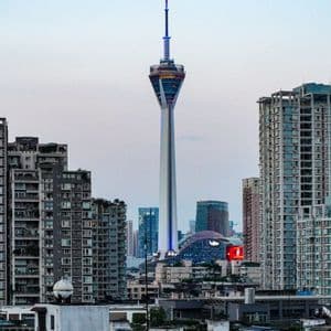 Una torre di osservazione alta e moderna si erge sopra una fitta città, piena di edifici residenziali, sotto un cielo pallido.