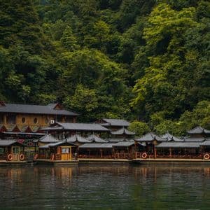 Barche turistiche con tetto a pagoda sono ormeggiate su un fiume tranquillo, davanti a una collina verde e lussureggiante, coperta di boschi.