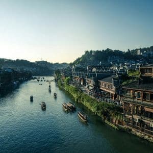 Una vista dall'alto di piccole barche su un fiume che attraversa un borgo tradizionale con edifici lungo le rive.