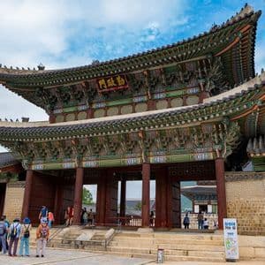 Un gruppo WeRoad in viaggio si trova in un cortile di fronte a un'ampia e sontuosa portineria tradizionale asiatica con un tetto a più livelli e decorato.