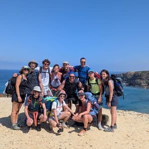 Un viaggio di gruppo WeRoad con zaini da trekking posa per una foto su una scogliera soleggiata a picco sull'oceano.