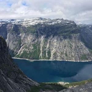 Montagne scoscese e rocciose, con cime innevate, circondano un fiordo blu intenso sotto un cielo nuvoloso.