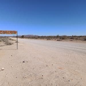 Un cartello 'Tropico del Capricorno' si erge accanto a una lunga strada sterrata in un vasto paesaggio desertico sotto un cielo azzurro.