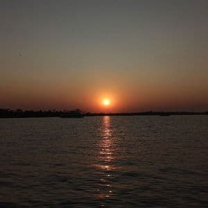 Il sole tramonta su un ampio specchio d'acqua, la sua luce arancione si riflette sulla superficie, con una barca visibile in lontananza.