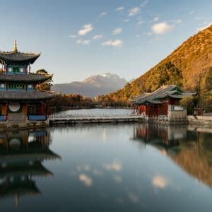 Eine traditionelle mehrstufige Pagode und ein Tempel auf einem ruhigen See, mit ihren Spiegelungen im Wasser und einem schneebedeckten Berg im Hintergrund.