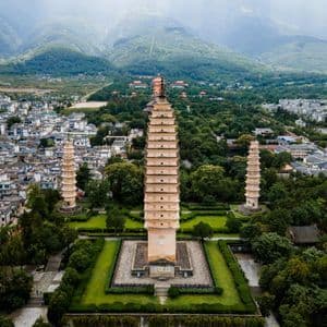 Una veduta aerea di tre pagode tradizionali immerse in un parco verde, circondate da una città ai piedi di montagne nebbiose.
