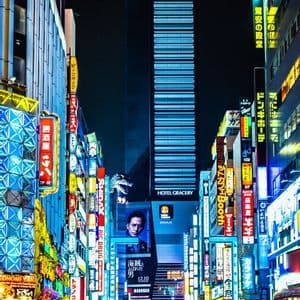Una strada cittadina animata di notte, affollata di persone e illuminata da vivaci insegne al neon su edifici imponenti.