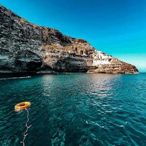 Un salvagente arancione galleggia sul mare turchese intenso accanto a una scogliera rocciosa sotto un cielo azzurro limpido.