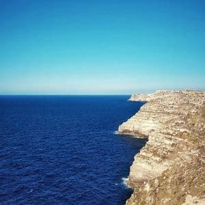 Una veduta dall'alto di aspre scogliere chiare che si affacciano su un mare blu profondo sotto un cielo azzurro limpido.