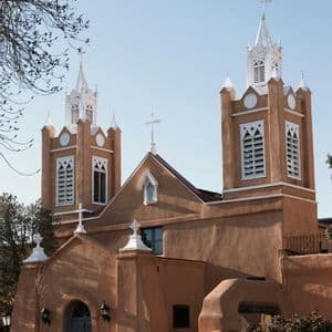 Una chiesa in stile adobe con due campanili gemelli dalla cima bianca si staglia contro un cielo azzurro e limpido.