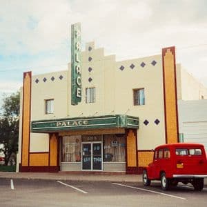 Un'auto rossa d'epoca parcheggiata davanti a un edificio in stile antico con un'insegna verticale verde che recita 'PALACE'.