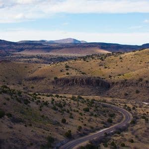 Una strada asfaltata che serpeggia tra colline aride e ondulate, punteggiate da arbusti verdi, ripresa da un punto panoramico elevato.