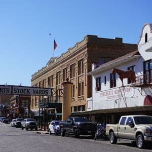 Il cartello d'ingresso dei Fort Worth Stock Yards si inarca su una strada di ciottoli fiancheggiata da auto ed edifici in stile western.