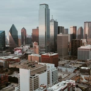 Veduta aerea di un denso skyline cittadino, ricco di moderni grattacieli di vetro, sotto un cielo coperto.