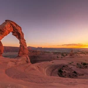 Un grande arco naturale in arenaria illuminato dalla luce calda di un'alba su un vasto paesaggio desertico.