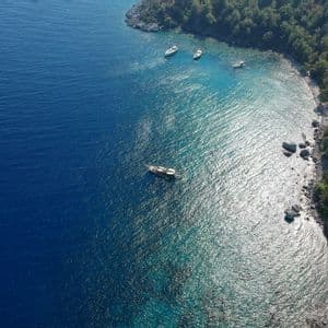 Una vista aerea di diverse barche ancorate in una baia turchese vicino a una costa rocciosa e alberata.