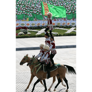 Un bambino sventola la bandiera del Turkmenistan dalla cima di una piramide umana formata da artisti equestri in abiti tradizionali.