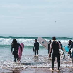 Un viaggio di gruppo WeRoad di surfisti in muta che trasportano le loro tavole e camminano tra le onde dell'oceano.