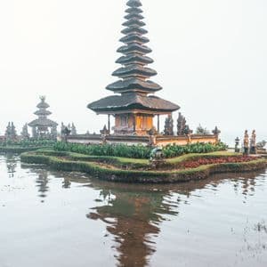 Un tempio asiatico a più livelli su una piccola isola circondata da acque calme, con il suo riflesso visibile in una giornata nebbiosa.