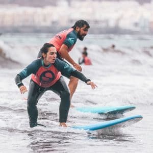 Un istruttore di surf aiuta una donna a bilanciarsi su una tavola da surf nell'oceano durante un viaggio di gruppo WeRoad.