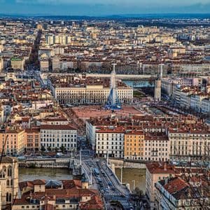 Veduta aerea di una vasta città europea con una grande piazza, una ruota panoramica, un fiume e un ponte in primo piano.