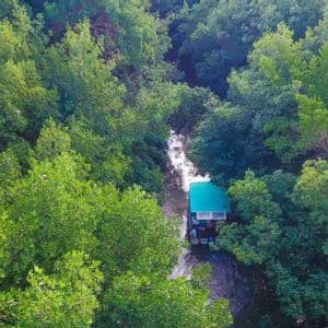 Vue aérienne d'un bateau au toit vert naviguant sur une rivière étroite, au cœur d'une forêt dense et luxuriante.