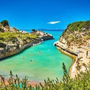 Le persone prendono il sole su scogliere rocciose e nuotano in una stretta insenatura di acqua turchese sotto un cielo azzurro e limpido.