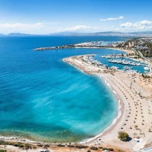 Vista aerea di una baia turchese con spiaggia sabbiosa, un porto turistico e una città costiera.