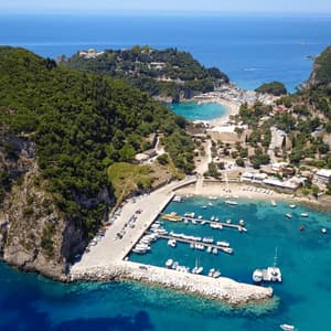 Una vista aerea di un porto con barche ormeggiate in acqua turchese, incastonato contro una costa verde e collinare.