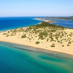Panoramica aerea di una penisola sabbiosa con vegetazione verde che separa le acque turchesi della costa da un mare blu intenso, con una montagna sullo sfondo.