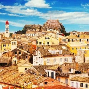 Una vista aerea dei tetti in terracotta di una città storica, con un campanile e una fortezza in cima a una collina sotto un cielo azzurro.