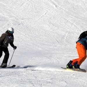 Un esquiador y un snowboarder, parte de un viaje en grupo de WeRoad, descienden por una ladera de montaña cubierta de nieve.