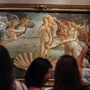 Museum visitors observe Botticelli's 'The Birth of Venus' in a large, gilded frame, with one person taking a photo.