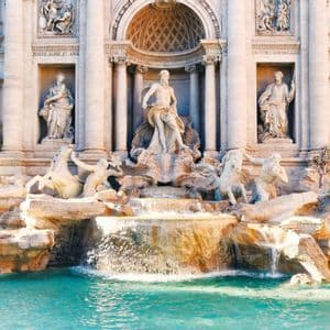 A grand white marble fountain featuring intricate sculptures of figures and horses, with water cascading into a turquoise pool.