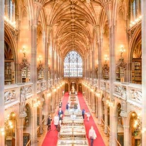 Vista dall'alto di persone che percorrono un tappeto rosso in una magnifica biblioteca storica con alti soffitti a volta e ricca architettura in pietra.