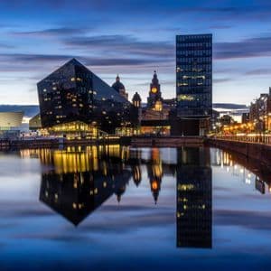 Uno skyline moderno con edifici illuminati che si riflettono nell'acqua calma di un porto al tramonto.