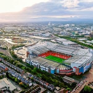 Una veduta aerea di Old Trafford, lo stadio del Manchester United, circondato dalla città circostante sotto un cielo nuvoloso.