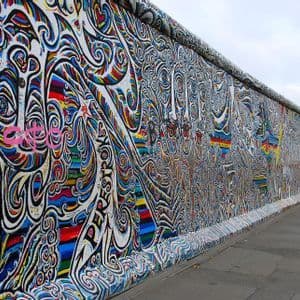 Un long mur de béton, recouvert de graffitis colorés et complexes, s'étend le long d'un trottoir sous un ciel gris.