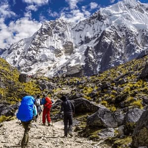 Un viaje en grupo de WeRoad camina por un sendero rocoso de montaña hacia un pico grande y cubierto de nieve bajo un cielo azul.