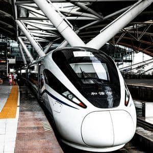 Un treno bianco ad alta velocità si è fermato sulla banchina di una stazione sotto un moderno tetto metallico geometrico.