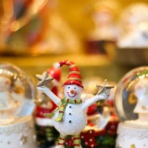 Una statuetta festiva di pupazzo di neve con un viso sorridente, che indossa cappello e sciarpa e regge due stelle.