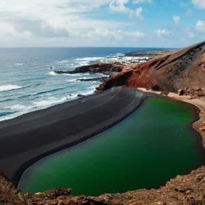 Una laguna verde separata dall'oceano da una spiaggia di sabbia nera ai piedi di una collina vulcanica.